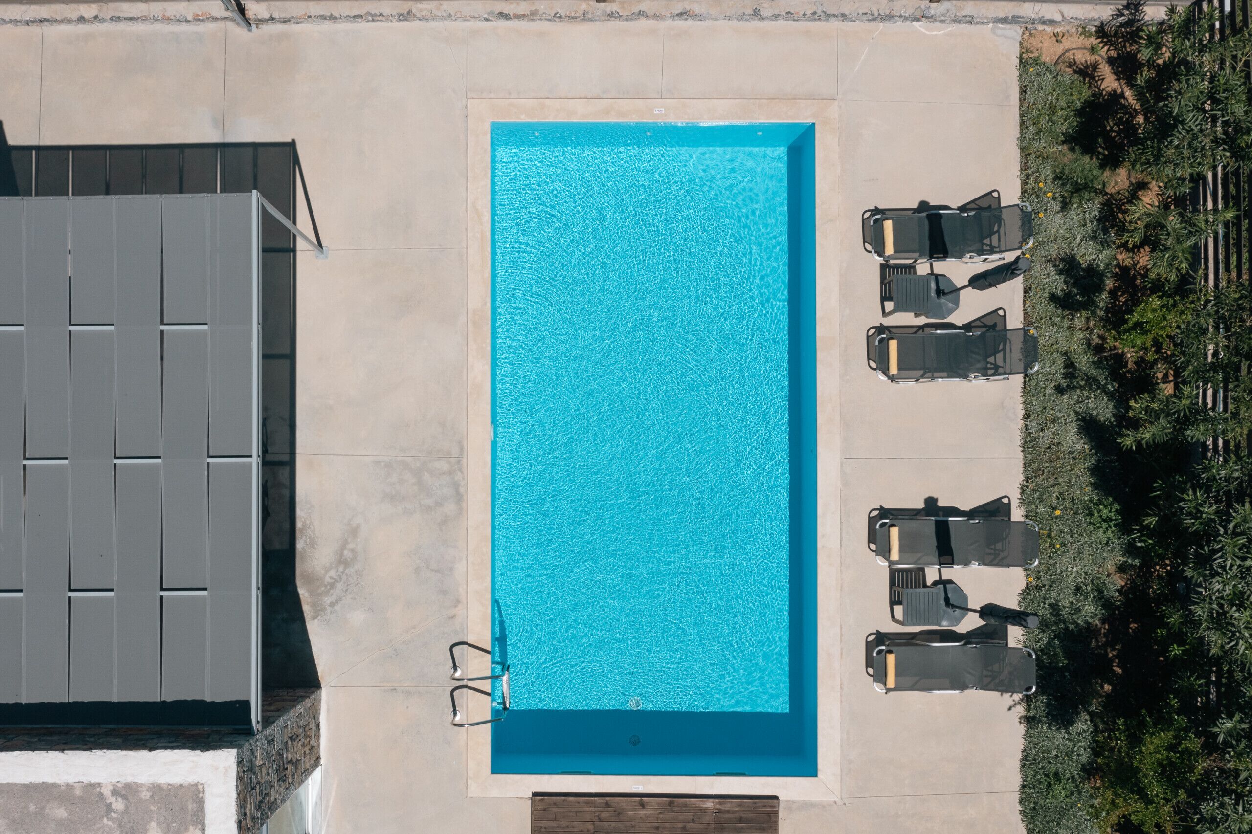 Vue aérienne d’une piscine rectangulaire, avec quatre chaises longues et un petit espace aménagé autour.