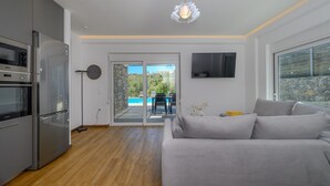 A modern kitchen with a built-in oven and microwave, a grey sofa, and a TV mounted on the wall. - Kalostous Villas (Rethymno)