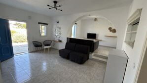 A modern living room with a sofa, a dining area with chairs, a TV, and a kitchen area with a refrigerator. - Villa Verdi Mykonos (mykonos)