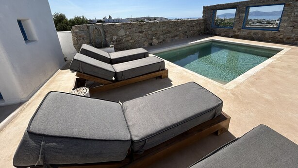 A rooftop pool with two lounge chairs and a stone wall. - Villa Verdi Mykonos (mykonos)
