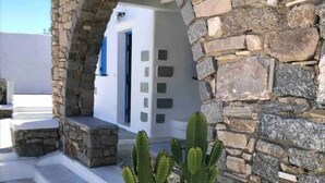 A stone archway leading to a white building with a door and windows, a cactus in a planter, and a white door with a metal handle. - Villa Verdi Mykonos (mykonos)