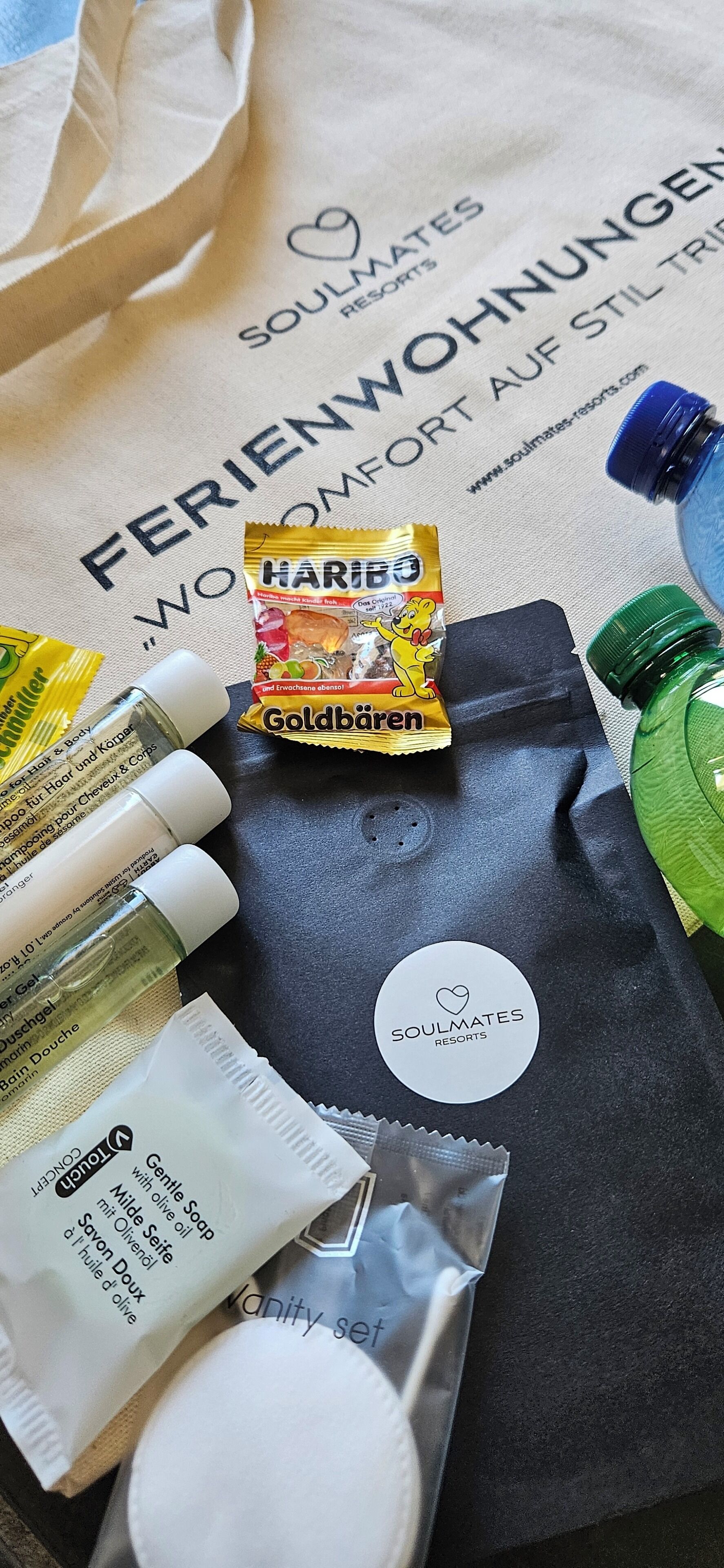 Toilettenartikel und eine schwarze Tasche mit weißem Etikett auf einer beigefarbenen Oberfläche.