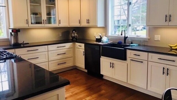 A kitchen with white cabinets, a black countertop, and a window providing natural light. - Beautiful home with large yard (Canton)