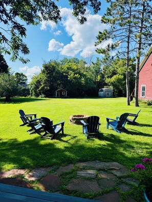 A grassy backyard with Adirondack chairs, a stone pathway, and a red building in the background.