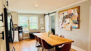 A spacious dining area with a wooden table and chairs, a kitchen in the background, and a bulletin board with various notes and pictures on the wall. - Beautiful home with large yard (Canton)
