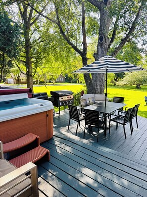 An outdoor deck with a hot tub, a grill, and a dining area with chairs and an umbrella. - Beautiful home with large yard (Canton)
