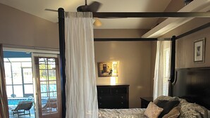 Un dormitorio con cama, mesita de noche, cómoda, ventilador de techo y ventana con cortinas.