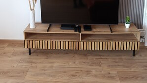A flat-screen TV on a wooden TV stand with a remote and a small plant.