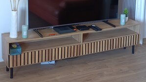 A flat-screen TV on a wooden TV stand with a remote, a small plant, and decorative items.
