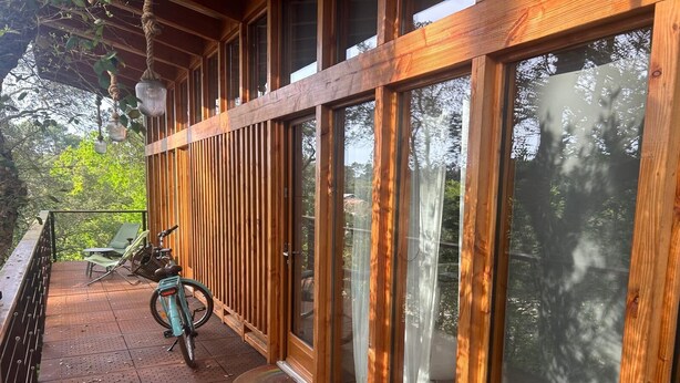 A wooden exterior with large glass doors, a bicycle, and a chair on a covered patio.