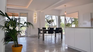 A modern kitchen with a dining area, large windows, and a potted plant. - The Beach House (Seignosse)