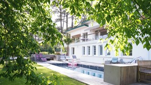 A poolside area with a wooden deck, lounge chairs, and a floating pool. - The Beach House (Seignosse)