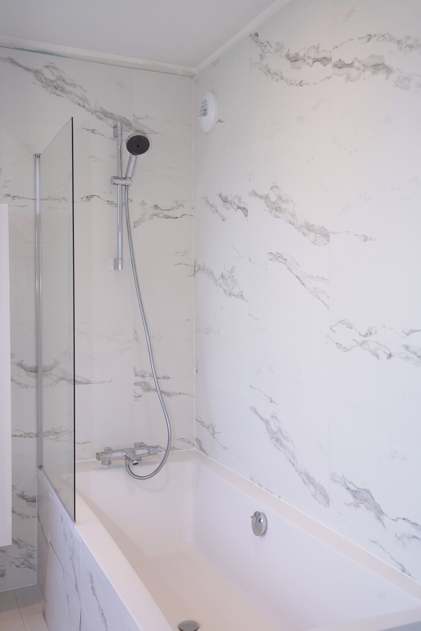 Un baño moderno con ducha envuelta en vidrio, una bañera independiente y paredes con diseño de mármol.