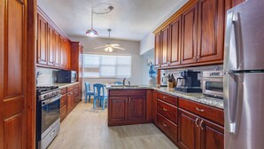 Una cocina con armarios de madera, electrodomésticos de acero inoxidable, una silla azul y un ventilador de techo.
