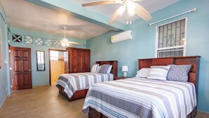 Un dormitorio con dos camas, piso de madera, ventilador de techo y aire acondicionado.