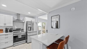 A modern kitchen with white cabinetry, stainless steel appliances, and a central island with two brown bar stools. - Charming Downtown Corner Cottage - 1 Block Walk to Food & Fun - Dog Friendly! (Southern Pines)