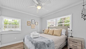 A bedroom with a bed, bedside tables, a ceiling fan, and windows with blinds. - Charming Downtown Corner Cottage - 1 Block Walk to Food & Fun - Dog Friendly! (Southern Pines)