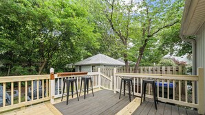 A wooden deck with a railing, surrounded by trees. - Charming Downtown Corner Cottage - 1 Block Walk to Food & Fun - Dog Friendly! (Southern Pines)