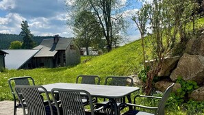 Une terrasse avec une table et des chaises, entourée de verdure et offrant une vue sur une maison et des arbres.