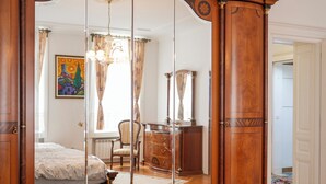 Une chambre avec un grand miroir, une armoire en bois et un lit recouvert d’une couvre-lit à motifs floraux.