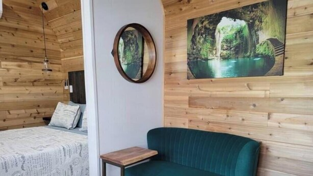 Een gezellige kamer met houten wanden, een bed met een beddegoed met dessin, een blauwgroene bank, een klein houten tafeltje en een lijst met een foto van een waterval.