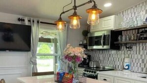 A modern kitchen with a central island, bar stools, a flat-screen TV, and a decorative vase. - 2 BM/French Country Style DPLX (Davenport)