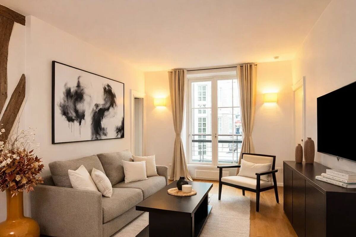 Un salon moderne avec un canapé gris, une table basse noire, un fauteuil blanc et un téléviseur posé sur un meuble.