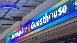 Egy színes dizájnnal és egy madár illusztrációjával ellátott, „Namtip Bar & Guesthouse” feliratú neonreklám.