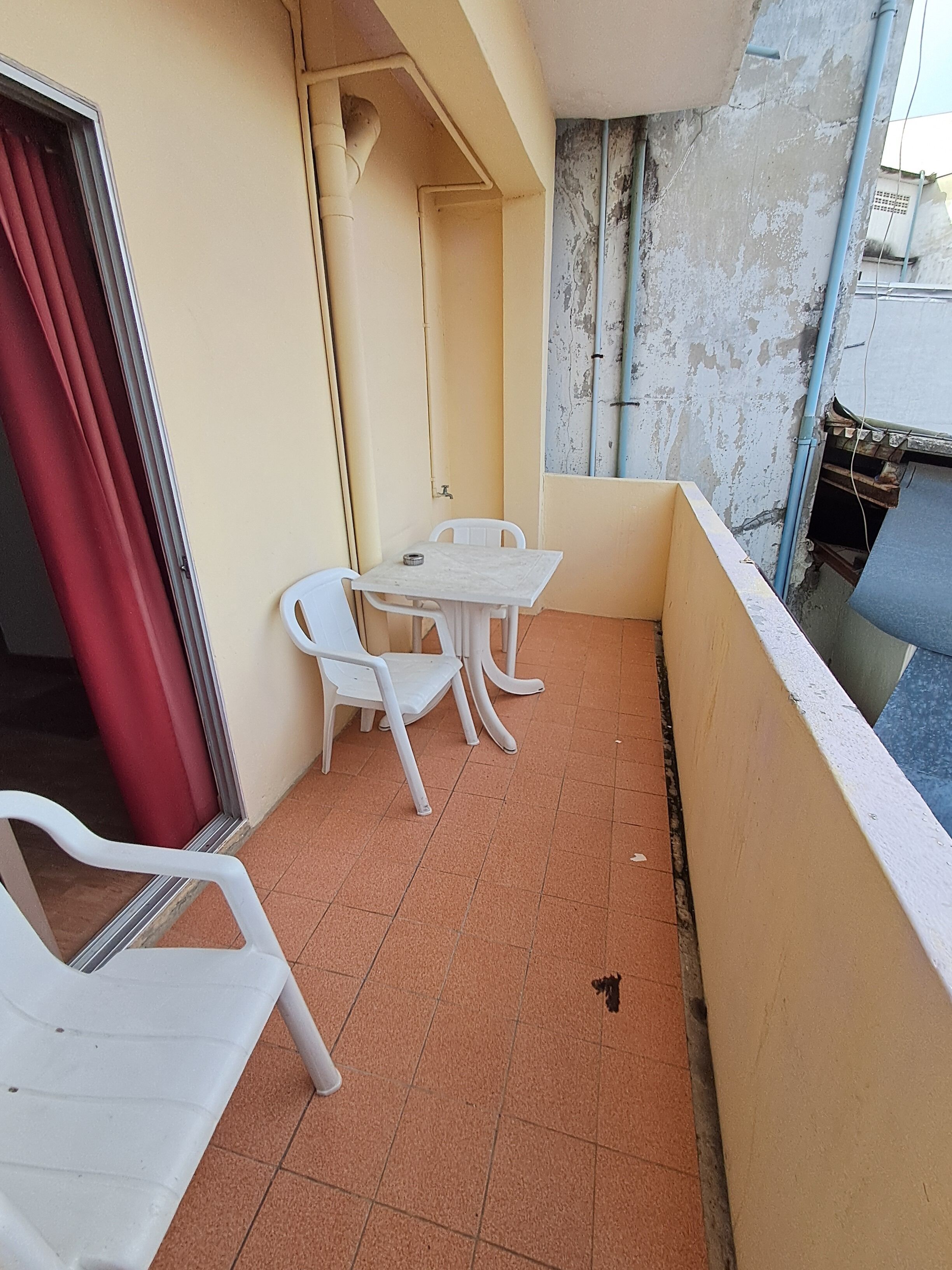 A small balcony with a table and chairs, a red curtain, and a tiled floor.