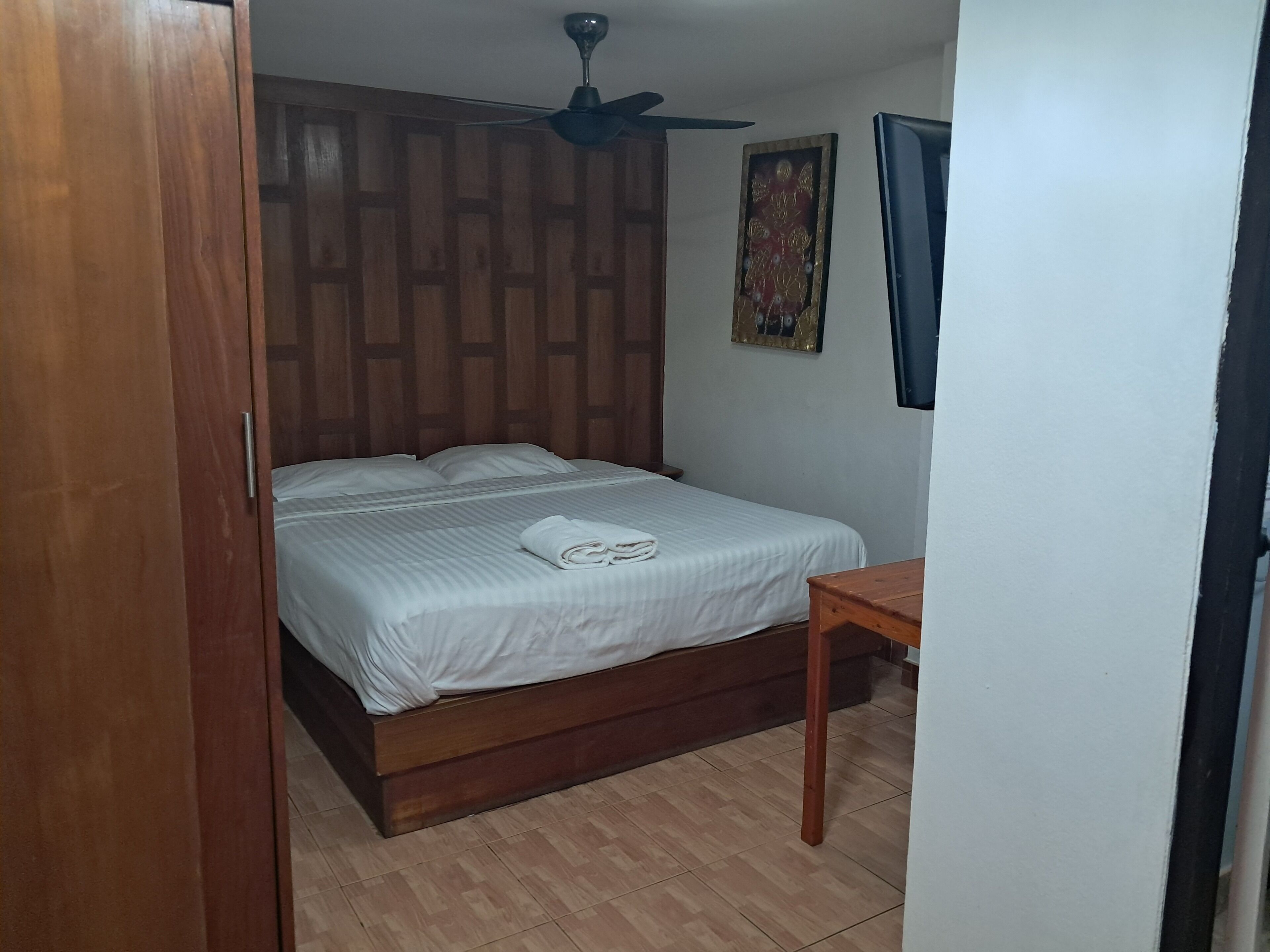 A bedroom with a wooden bed, a ceiling fan, a small table, and a wall-mounted picture.