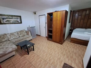 A living room with a sofa, a coffee table, a wardrobe, and a bed. - Namtip Bar & Guesthouse (Pattaya)