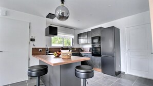 A modern kitchen with a central island, black bar stools, a stainless steel refrigerator, and a pendant light.