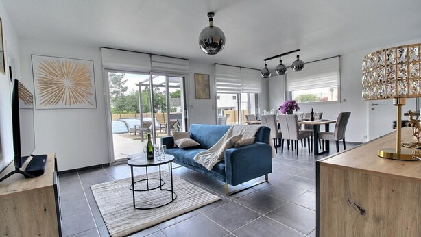 A modern living room with a blue sofa, a round coffee table, and a dining area with a table and chairs.
