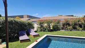 A swimming pool with lounge chairs, a well-maintained lawn, and a building with a tiled roof in the background. - Air-conditioned villa with swimming pool between the sea and the Cevennes mountains. (La Calmette)