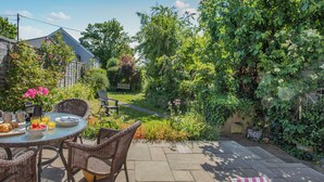 A patio with a table set for breakfast, wicker chairs, and a garden view. - Welcome to this delightful fisherman’s cottage on the unique Island of Mersea. (Mersea Island)