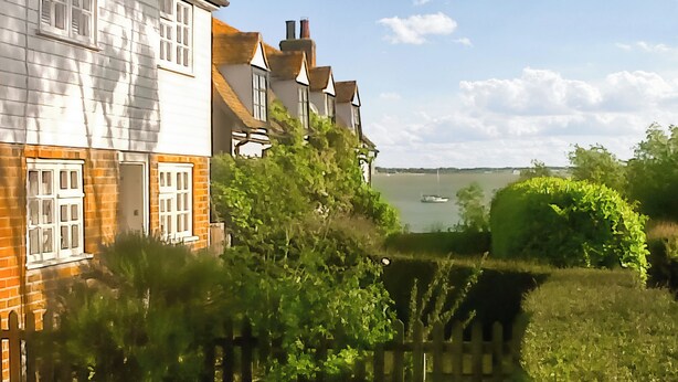 A residential area with houses, a wooden fence, and a body of water in the background. - Welcome to this delightful fisherman’s cottage on the unique Island of Mersea. (Mersea Island)