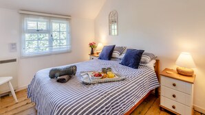 A neatly made bed with a tray of breakfast, a bedside table with a lamp, and a window with blinds. - Welcome to this delightful fisherman’s cottage on the unique Island of Mersea. (Mersea Island)
