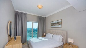 Hotelkamer met een bed, een bureau, een stoel, een lamp, een schilderij en uitzicht op de stad.