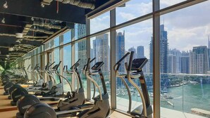 Un gimnasio con cintas de correr y pesas, amplias ventanas y vistas a la ciudad.