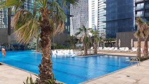 Piscina con palmeras y sillas de descanso, rodeada de edificios modernos.