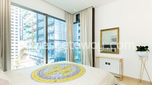 Una habitación de hotel moderna con un ventanal grande, una cama con cubrecama estampado, un espejo con marco dorado y una planta en maceta.