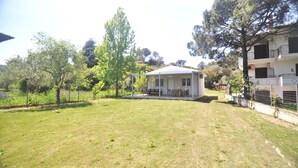 A house with a covered porch, surrounded by a grassy yard and trees. - Zennova 29 Vourvourou Garden House (Vourvourou)