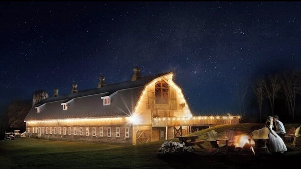A large barn-like building with a sloped roof and multiple chimneys, illuminated by warm lights. - Large tent on massive Big Rock Creek Estate! (Saint Croix Falls)