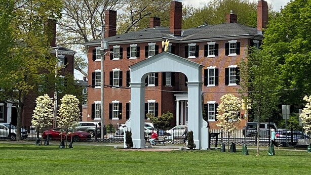 A large brick building with a central white archway, surrounded by a well-maintained lawn and trees.