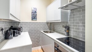 A compact kitchen with white cabinets, a stainless steel sink, and a black induction cooktop.