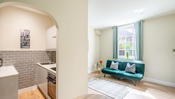 A modern kitchen with a brick backsplash, a white countertop, and a built-in oven. There is a window with curtains and a green sofa in the living area.