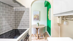 A modern kitchen with a black stovetop, grey tiled backsplash, and a round wooden table with two chairs.