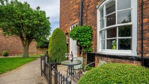 A brick building with a large window, a small table with chairs, and a well-maintained garden.