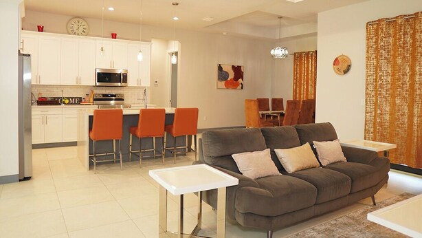 Una sala moderna con un sofá gris, sillones naranjas y una mesa de centro blanca.