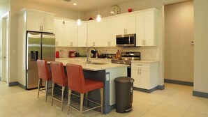 Una cocina moderna con gabinetes blancos, electrodomésticos de acero inoxidable y una isla central con taburetes de bar.